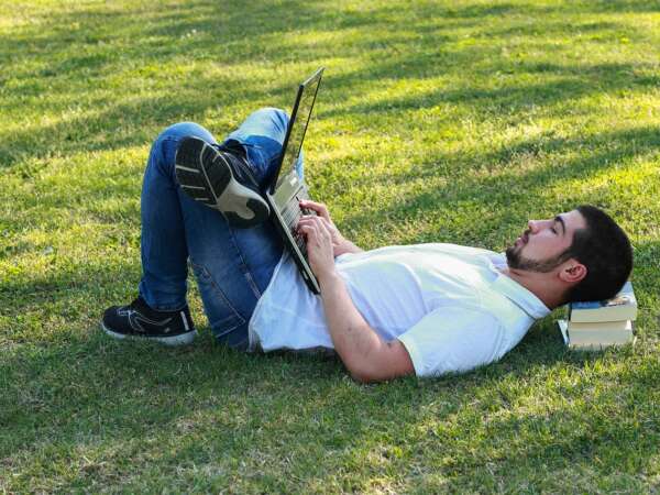 Man lies in the park working on a laptop