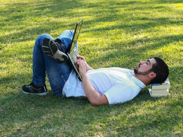 Man lies in the park working on a laptop