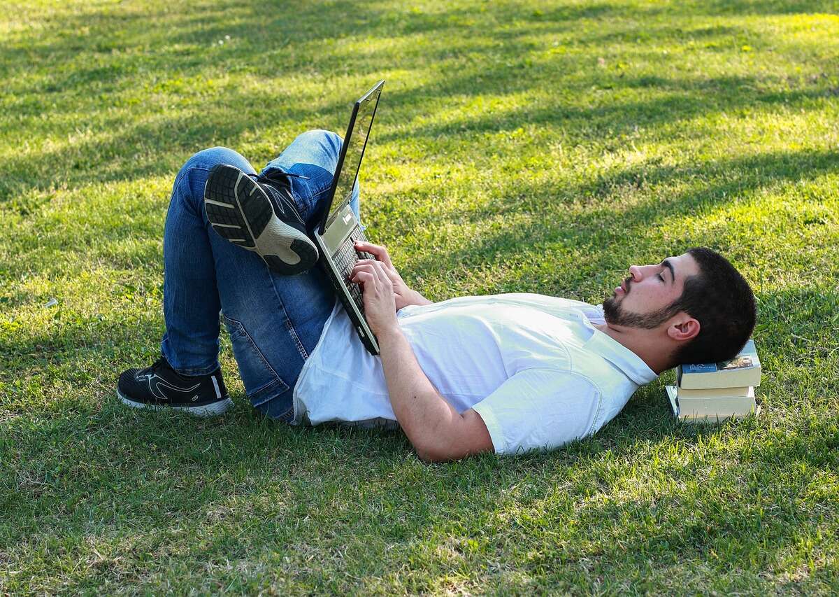Man lies in the park working on a laptop